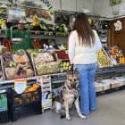 Un perro guía con su usuaria en una frutería.