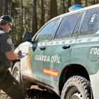 Agente de la Benemérita junto a un vehículo policial en un monte.