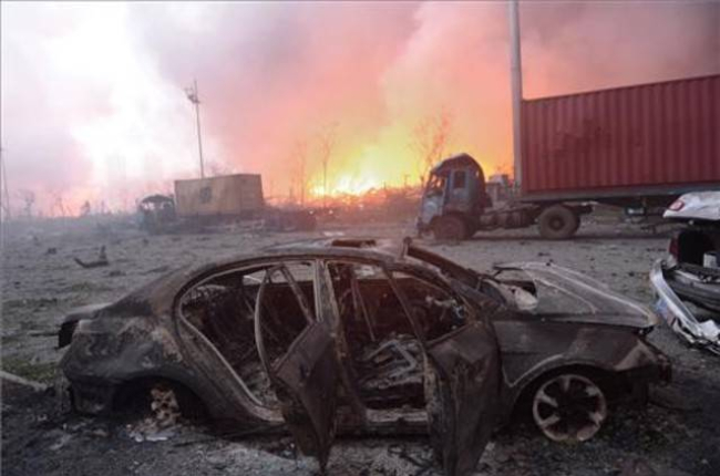 Vista de un coche calcinado en la seria de explosiones de unos almacenes de Tianjin, en China. En segundo plano, el fuego sigue ardiendo.-AFP / TIANJIN