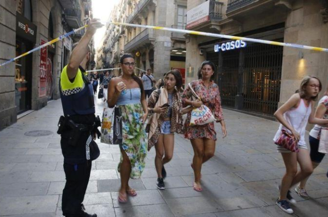 Unos turistas pasan bajo un cordón policial en la calle de Portaferrissa.-ÁLVARO MONGE