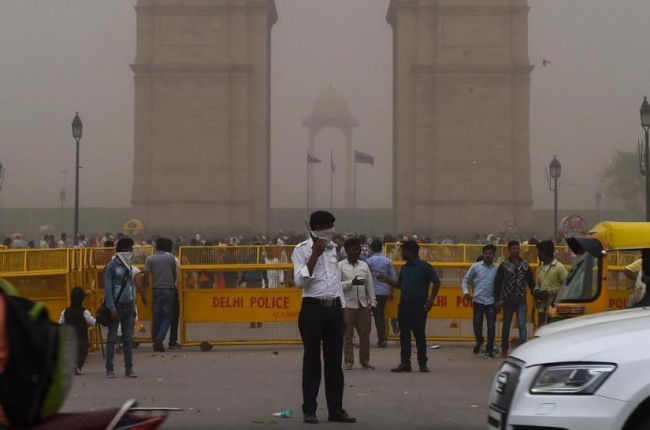 Un agente de policía de Nueva Delhi dirige el tráfico mientras se cubre la cara en medio de una tormenta de arena.-/ CHANDAN KHANNA (AFP)