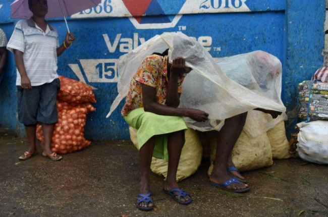 Unas mujeres se protegen de la lluvia con un plástico en la capital de Haití, Port-au-Prince.-ARCHIVO / AFP