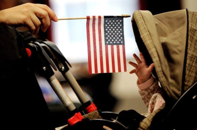 Imagen muestra a un bebe que intenta alcanzar la bandera estadounidense que sostiene su madre en Nueva York.-EPA