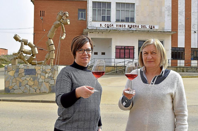 De izquierda a derecha, Marta Fernández y Mariló Maroto, con el rosado de la cooperativa, ante la escultura que rinde homenaje a los hombres y mujeres que construyeron las bodegas subterráneas de Valderas y plantaron sus viñas.-ARGI