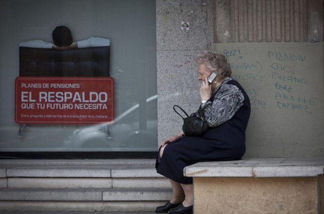 Una mujer mayor habla por teléfono móvil al lado de un cartel de planes de pensiones.-MIGUEL LORENZO