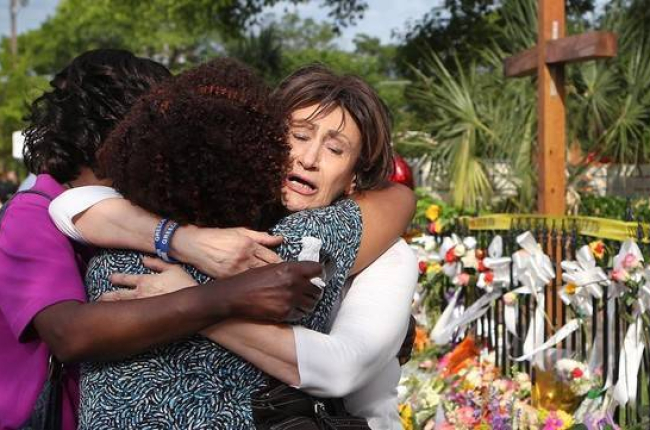 Tres mujeres se abrazan junto a la ofrenda floral frente a la iglesia metodista, en Charleston, este sábado.-Foto:   AP / CURTIS COMPTON