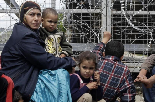 Un mujer migrante rodeada de niños, sentados junto a una valla durante una protesta por las penosas condiciones del campo de refugiados y contra el cierre del paso fronterizo de Idomeni (Grecia), este jueves.-AP / GREGORIO BORGIA