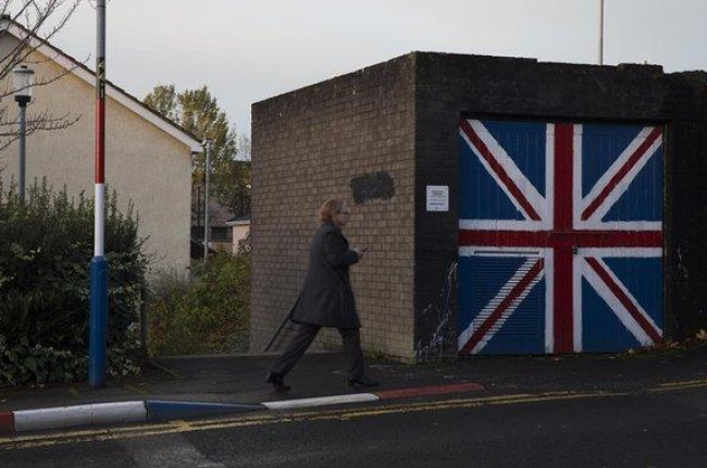 Una mujer pasa junto a un muro que luce la bandera de la Union Jack, en el barrio de Fountain West, en la localidad norirlandesa de Derry.-ALBERT BERTRAN