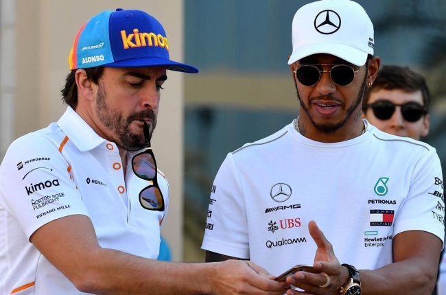 Alonso consulta un móvil junto a Hamilton en Abu Dhabi.-AFP