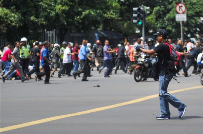Un hombre armado apunta hacia un centro comercial mientras decenas de personas corren, en el centro de Yakarta.-AP / VERI SANOVRI
