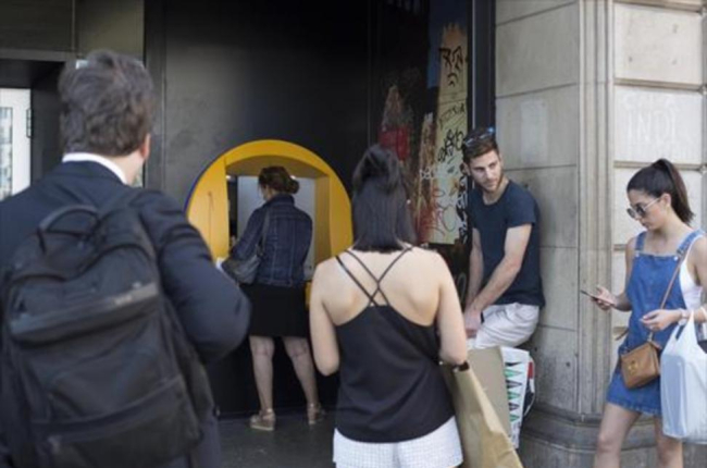 Varias personas esperan para operar en un cajero de una oficina de CaixaBank en la plaza de Catalunya.-ALBERT BERTRAN
