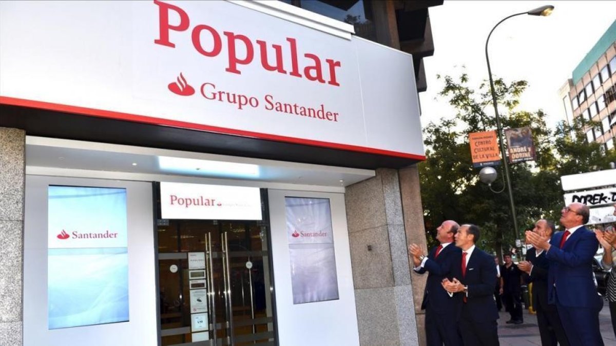 Directivos del Santander ante una de las primeras oficinas del Popular que ya ha adoptado la imagen corporativa del grupo cántabro, en Madrid-EL PERIÓDICO