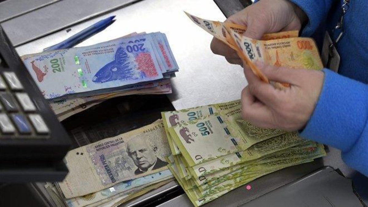 Un cajero cuenta billetes de pesos en un supermercado de Buenos Aires, el pasado jueves.-JUAN MABROMATA (AFP)