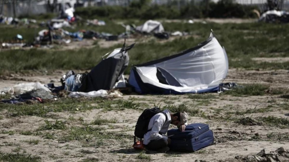 Un kurdo espera sentado junto a su maleta el momento de abandonar Idomeni.-AP / YANNIS KOLESIDIS