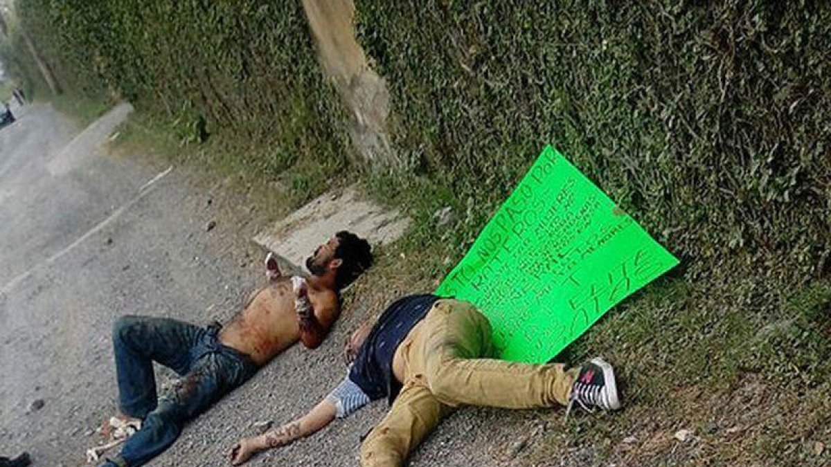 Dos de las víctimas en el suelo, junto a un cartel que les acusa de ladrones, firmado por un grupo de justicieros, este lunes en Guadalajara (México).-EFE