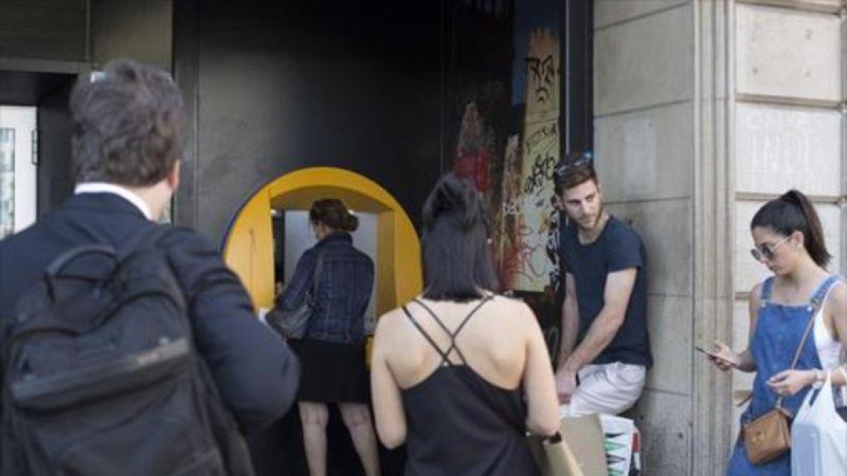 Varias personas esperan para operar en un cajero de una oficina de CaixaBank.-ALBERT BERTRAN