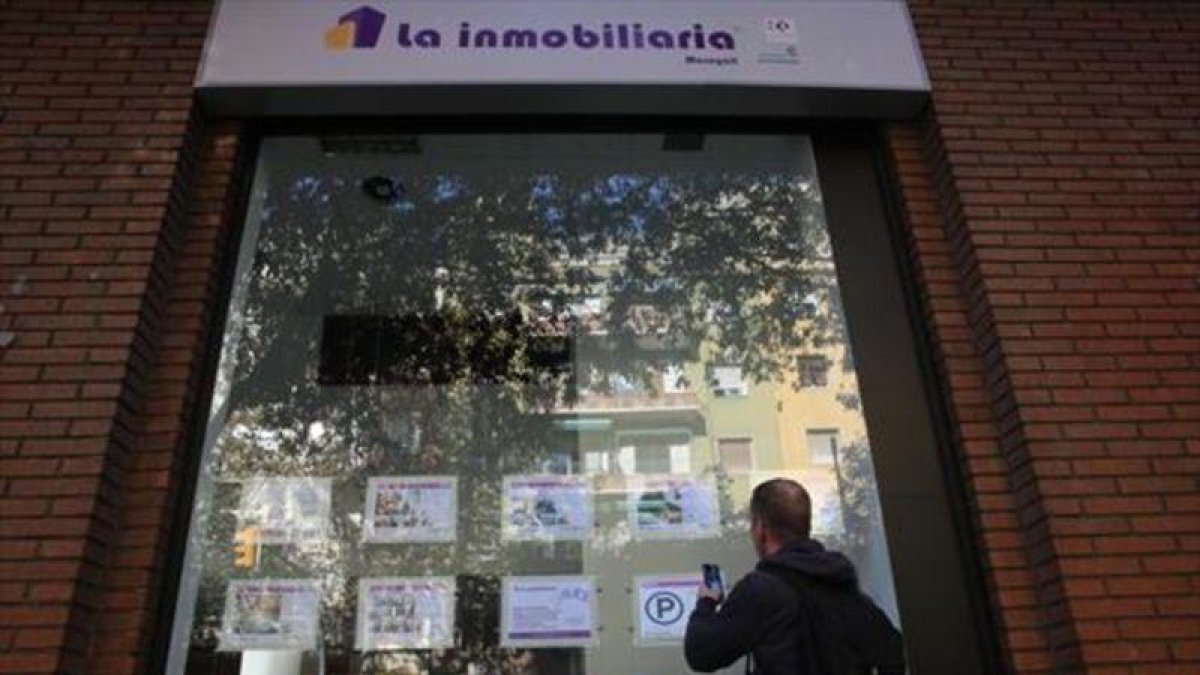 Un joven toma nota de una de las ofertas de pisos disponibles en alquiler en una agencia de Barcelona, esta semana.-ELISENDA PONS