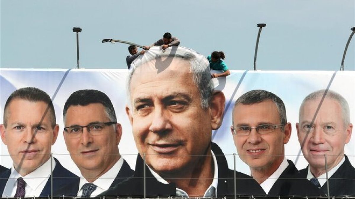 Un grupo de operarios trabaja en una valla publicitaria de propaganda electoral en la que aparece Netanyahu con candidatos de su partido, el Likud, en Jerusalén.-REUTERS / AMMAR AWAD