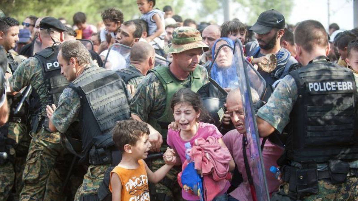 Varios refugiados ayudan ayer a uno de sus compañeros que muestra su desesperación con un niño en brazos frente a la policía de Macedonia.-Foto: AP/ D. V.