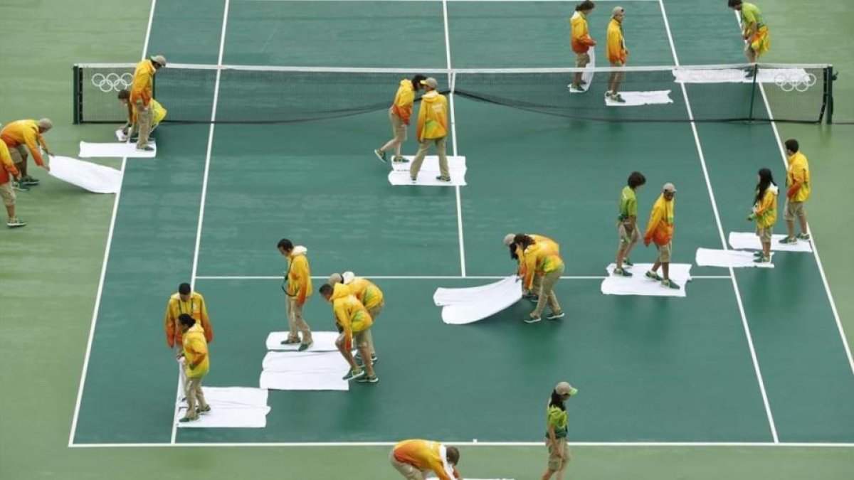 Voluntarios secan con toallas la pista central, en Río de Janeiro.-EFE / MICHAEL REYNOLDS