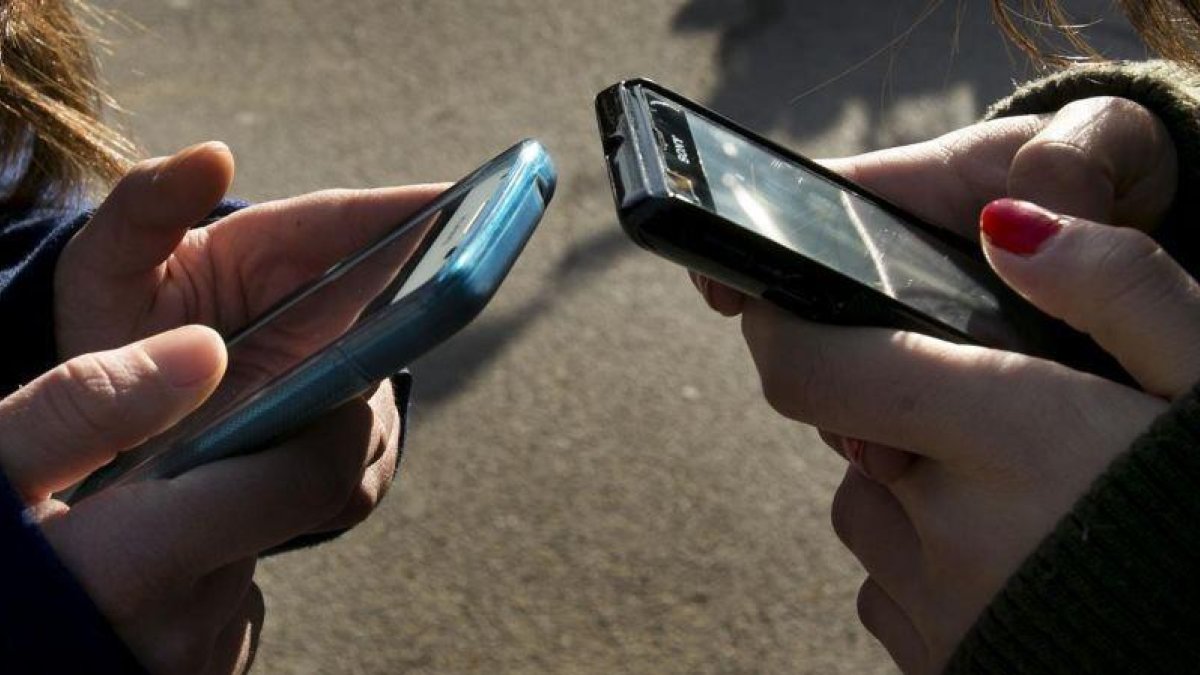 Una foto de archivo con dos personas escribiendo en sus teléfonos móviles.-FERRAN NADEU
