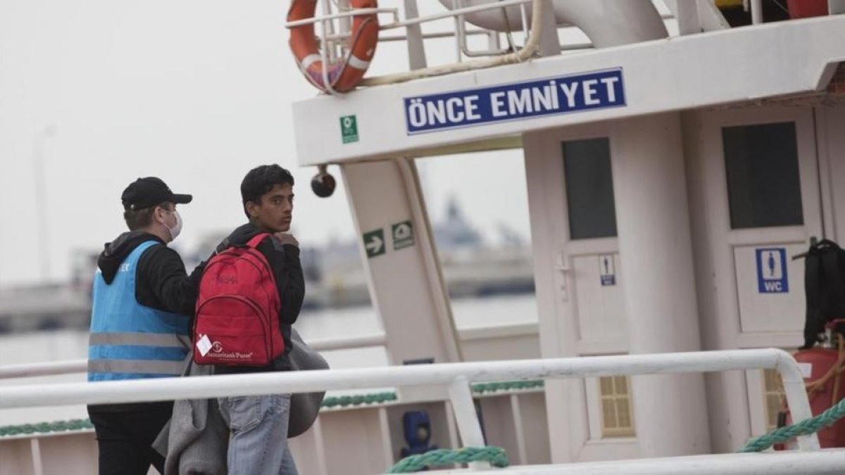 Un migrante pakistaní mira hacia atrás, conducido por un funcionario, en el ferri a punto de partir hacia Turquía, en Lesbos, este viernes.-AP / PETROS GIANNAKOURIS