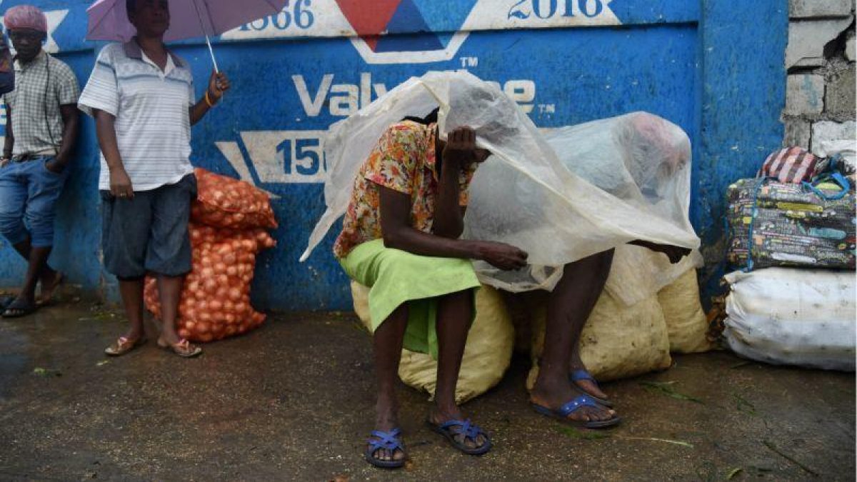 Unas mujeres se protegen de la lluvia con un plástico en la capital de Haití, Port-au-Prince.-ARCHIVO / AFP