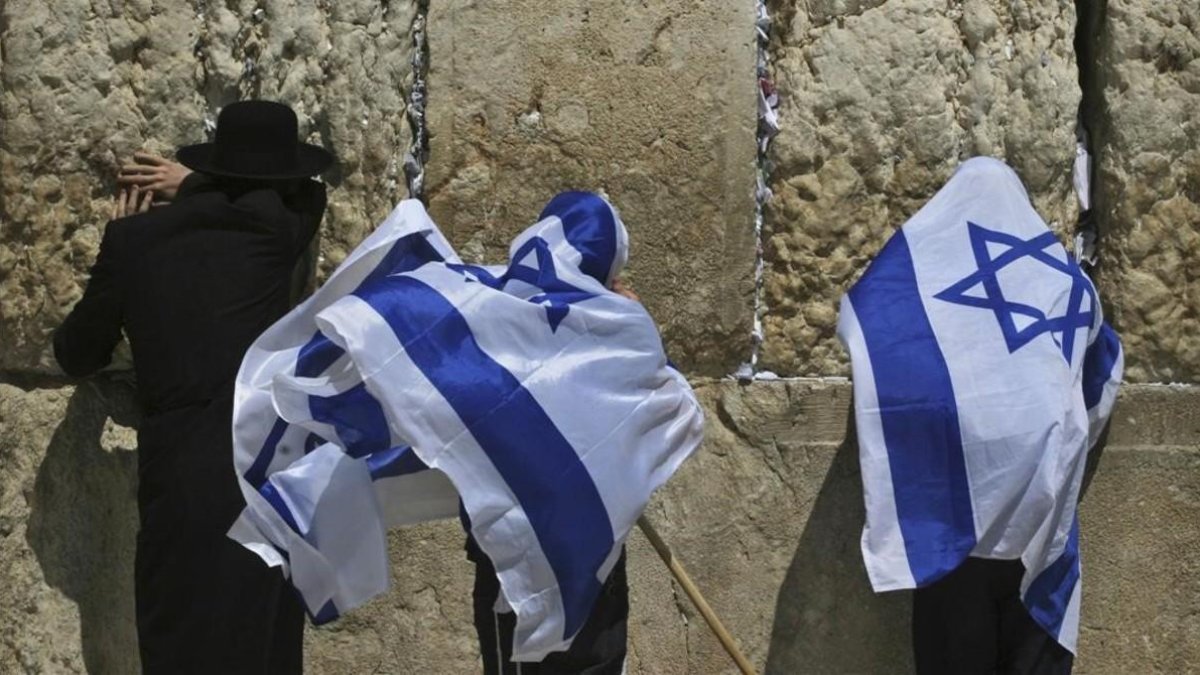 Jóvenes israelís se cubren con la bandera de Israel junto a un untraortodoxo frente al Muro de las Lamentaciones. /-AP / DAN BALILTY