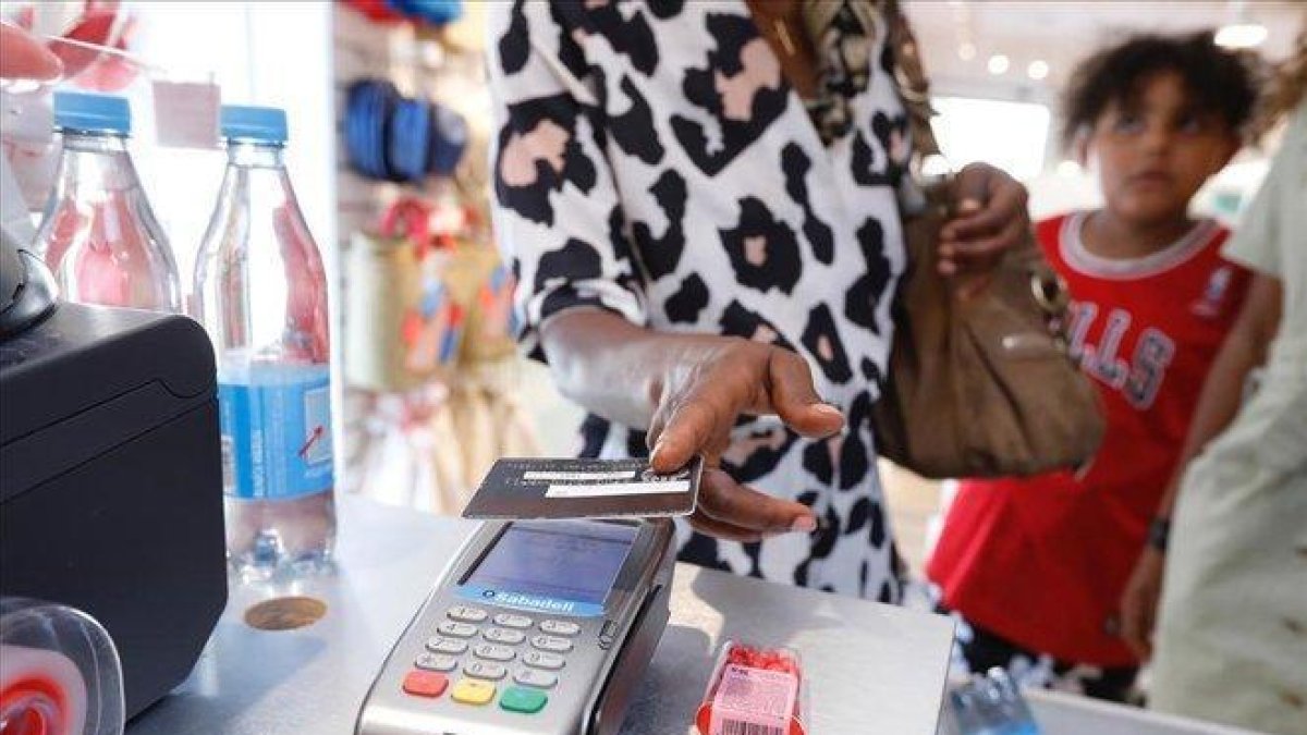 Una consumidora paga con trjeta en una tienda de ropa.-