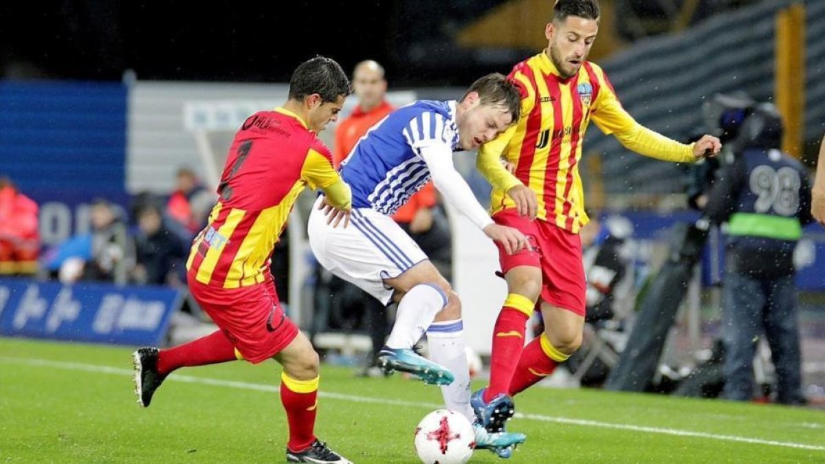Bautista, de la Real, pelea un balón entre dos jugadores del Lleida.-EFE / GORKA ESTRADA