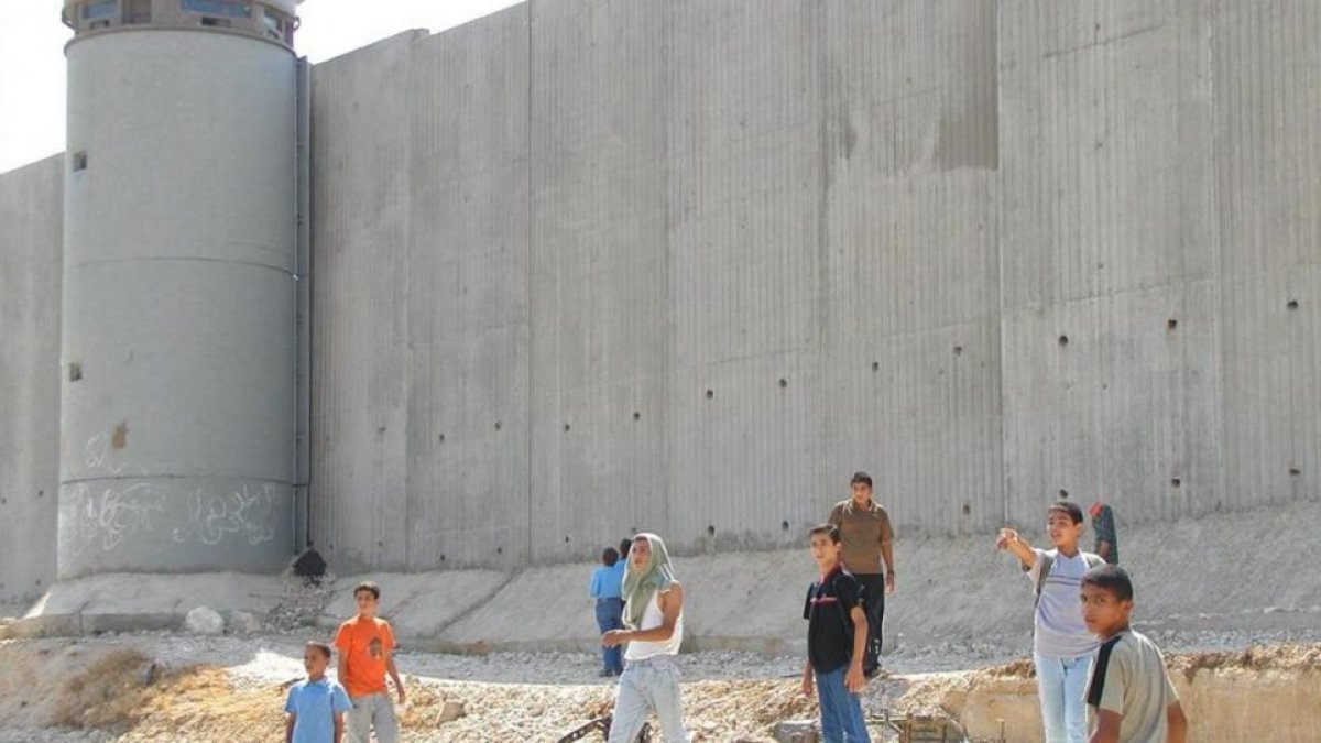 Niños palestinos de camino a la escuela, junto al muro construido por Israel cerca de Qalqilya (Cisjordania).-AP / MOHAMMED AZBA