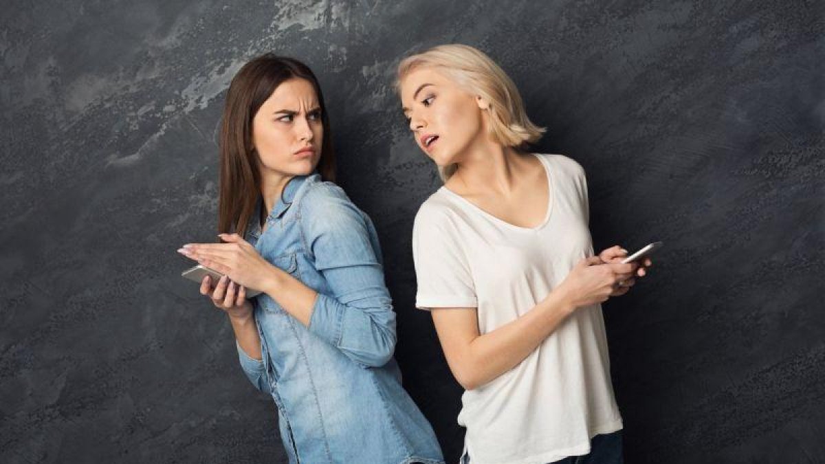 Una chica espía el móvil de su amiga.-123RF