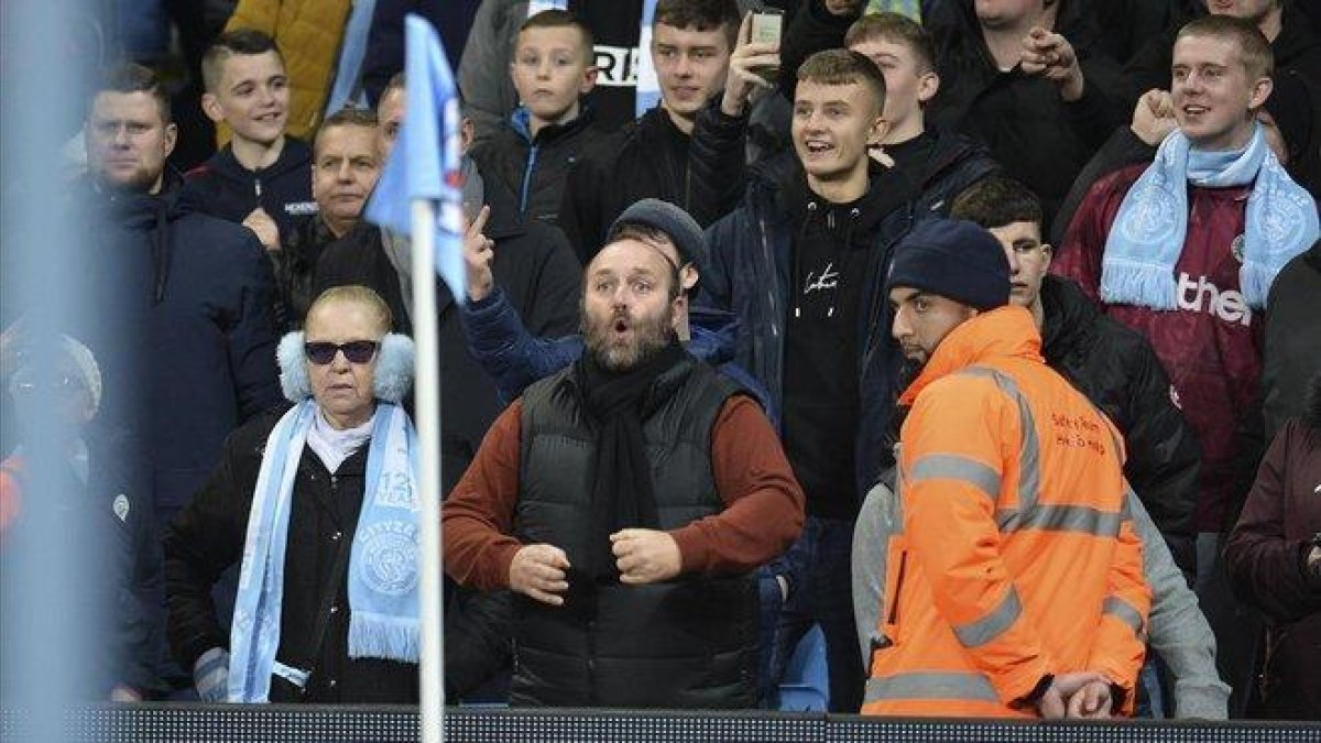Un aficionado del Manchester City hace gestos racistas a los jugadores del United.-EFE / PETER POWELL