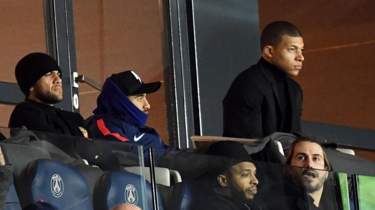MBappé, abrigado, siguiendo el último partido del PSG, junto a Dani Alvés, en el Parque de los Príncipes.-AFP