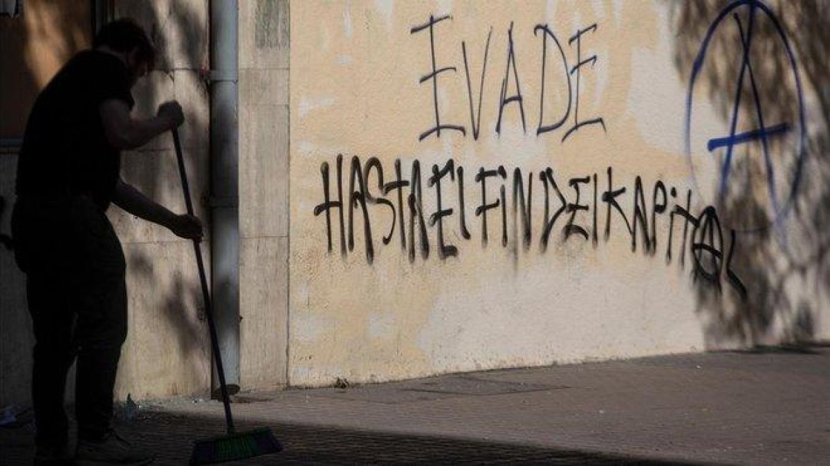 Un hombre barre el suelo ante un grafiti que reivindica la ’evasión’, en una calle de Santiago de Chile.-CLAUDIO REYES (AFP)