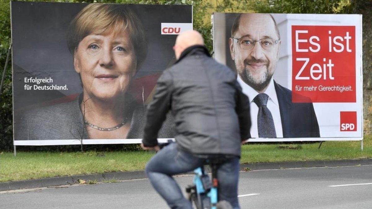Un ciclista pasa frente a dos carteles electorales de Merkel (izquierda) y Schulz, en Essen, el 14 de septiembre.-AP / MARTIN MEISSNER