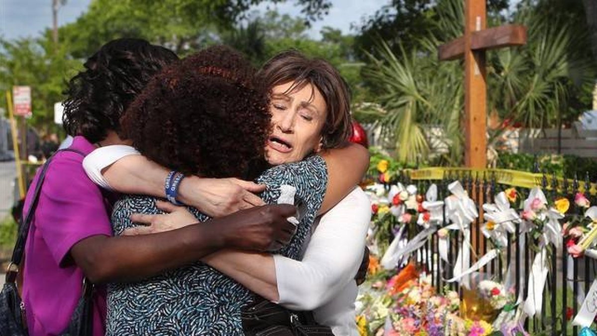 Tres mujeres se abrazan junto a la ofrenda floral frente a la iglesia metodista, en Charleston, este sábado.-Foto: AP / CURTIS COMPTON