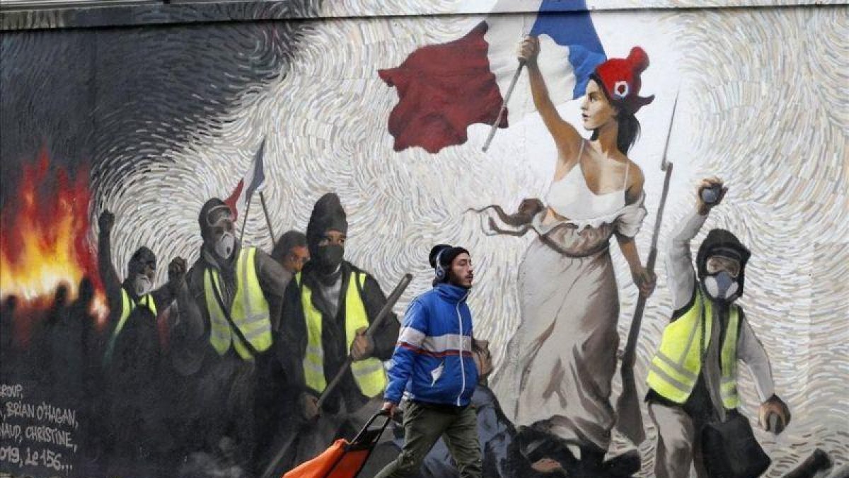 Un hombre pasa junto a un mural que reproduce una versión de La libertad guiando al pueblo, de  Eugene Delacroix, con la presencia de chalecos amarillos, idea del artista Pascal Boyart.-GETTY IMAGES