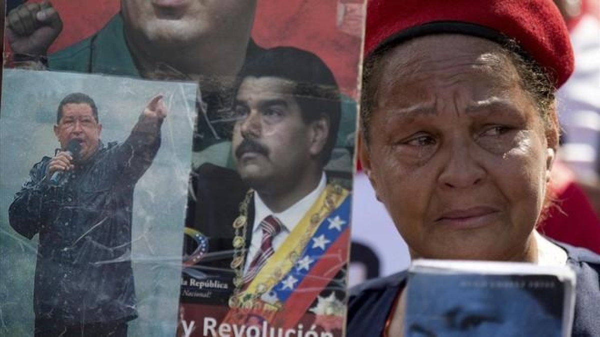 Una partidaria del chavismo llora mientras sostiene imágenes de Chávez y Maduro, durante una marcha por el quinto aniversario de la muerte de Chávez, en Caracas, el 15 de marzo.-AP / FERNANDO LLANO