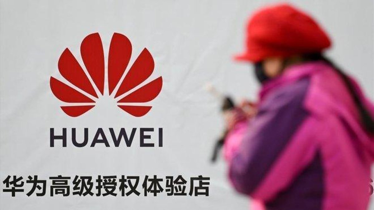 Una mujer consulta su smartphone junto a un cartel publicitario de Huawei, en una calle de Pekín.-WANG ZHAO (AFP)