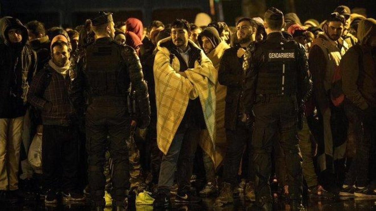 Un grupo de foráneos esperan un autobús para su traslado durante una operación de desalojo de campamentos de migrantes en París.-JULIEN DE ROSA (EFE)
