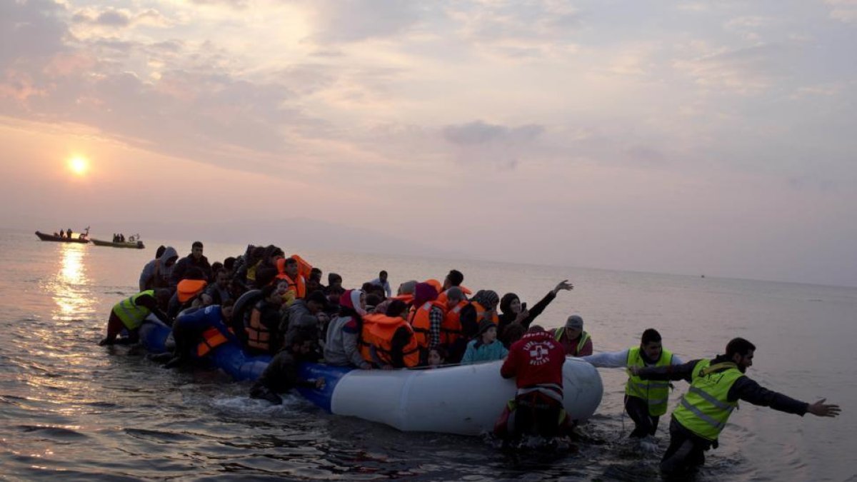 Varios voluntarios ayudan a un grupo de refugiaos a llegar a la costa, en la isla griega de Lesbos, el pasado marzo.-AP