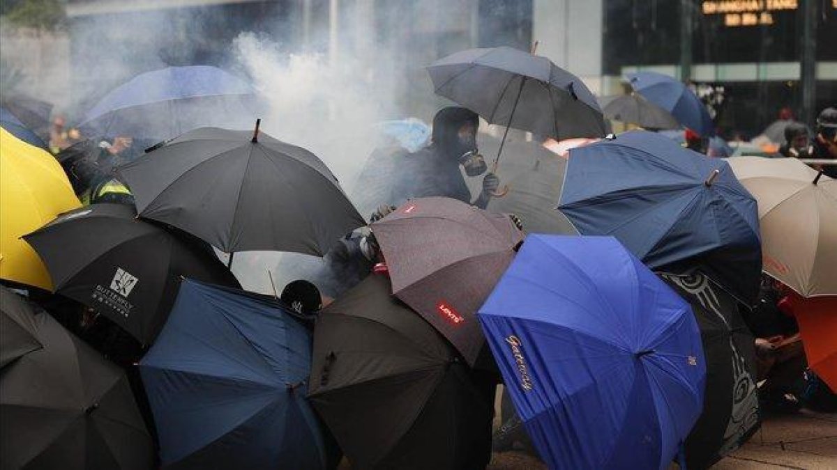 Varios manifestantes se protegen con paraguas de los gases lacrimógenos lanzados por la policía, este domingo en Hong Kong.-AP / / VINCENT THIAN