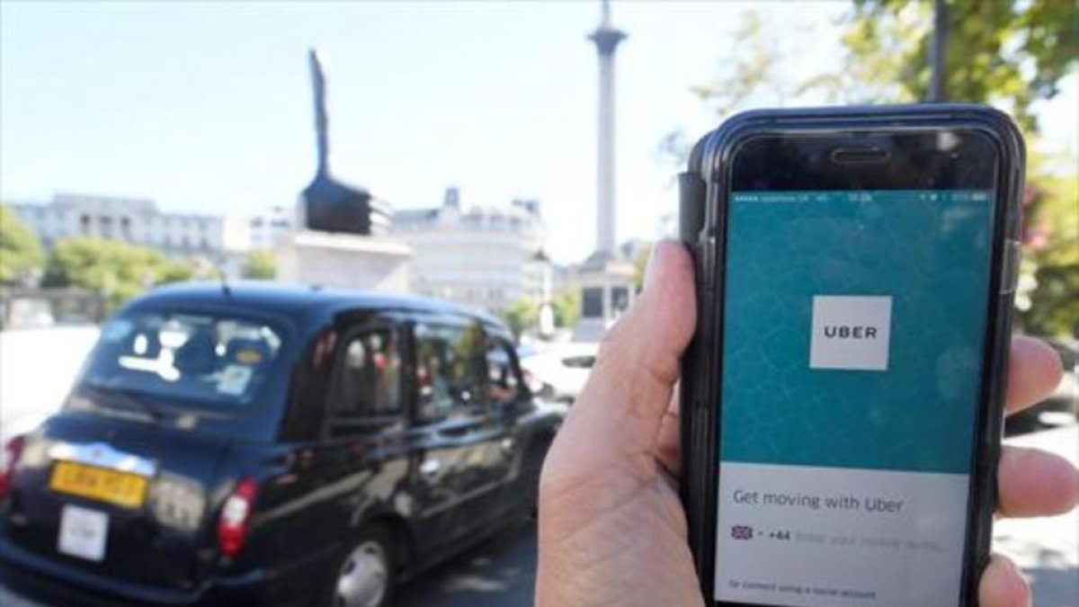 Un taxi de Londres pasa delante de un móvil con la aplicación de Uber activada, ayer.-REUTERS / TOBY MELVILLE