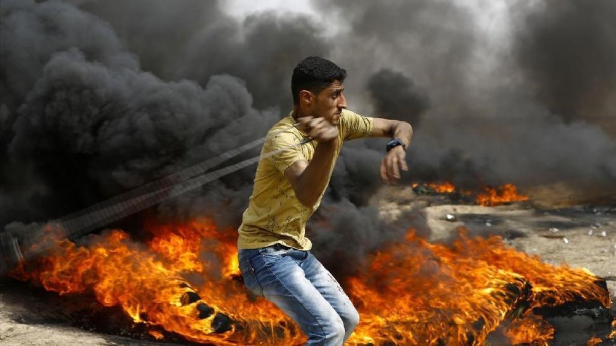 Un palestino se dispone a lanzar piedras entre los neumáticos incendiados contra las tropas israelís, en las protestas junto a la frontera de la Franja de Gaza, el 20 de abril.-MOHAMMED ABED