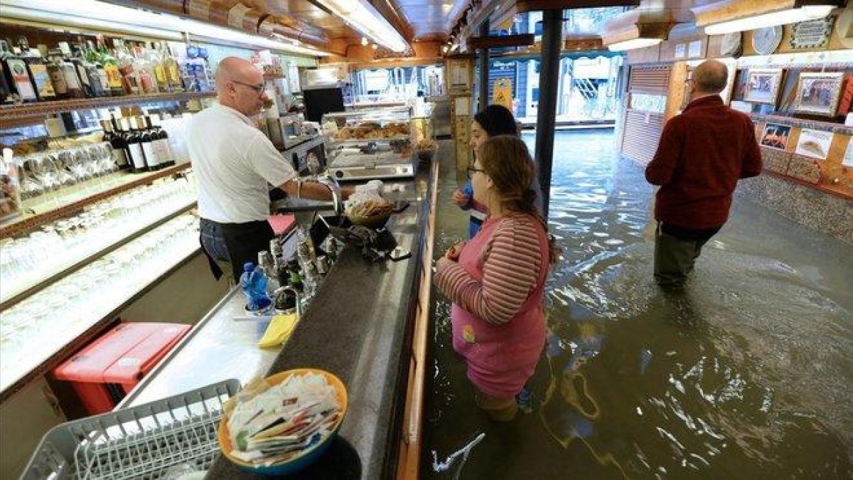 Clientes de un bar, con el agua hasta por encima de las rodillas, este domingo.-AP / ANDREA MEROLA