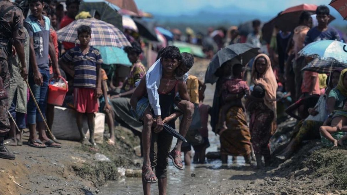 Un joven refugiado rohingya lleva a cuestas un hombre mayor en una zona cercana al lado bangladesí de la frontera con Birmania, tras cruzar el río Naf, el 17 de octubre.-AFP / MUNIR UZ ZAMAN
