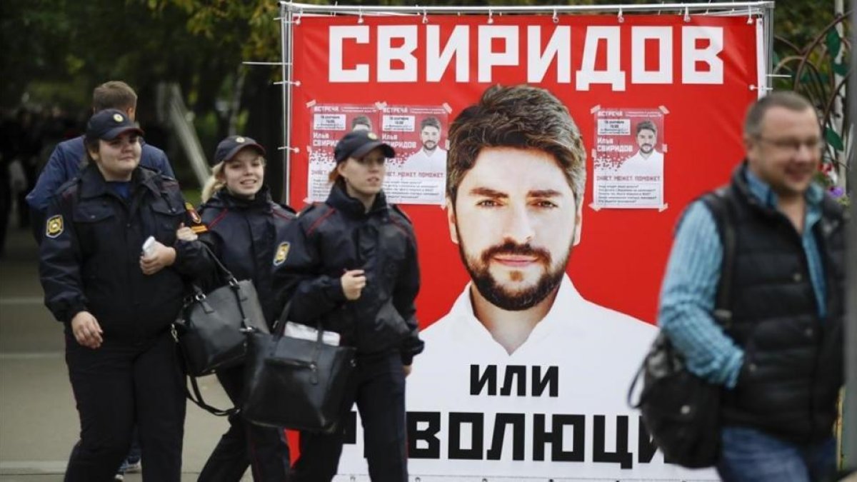 Varias personas pasan junto a un póster electoral del partido nacionalista Rodina (Patria), en Moscú, este jueves.-AP / PAVEL GOLOVKIN