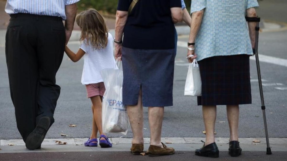 Tres generaciones de ciudadanos a la espera de cruzar una acera.-JULIO CARBO