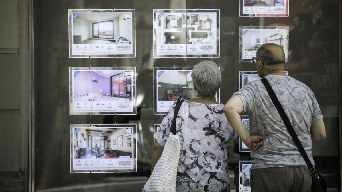 Una pareja chequea pisos de alquiler en una inmobiliaria.-JOAN CORTADELLAS